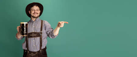 Portrait of bearded man in traditional Bavarian costume with one liter of dark beer isolated over green background. Octoberfest, Festival conceptの写真素材