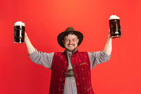 Happy smiling man dressed in traditional Austrian or Bavarian costume holding two mugs, glasses of...