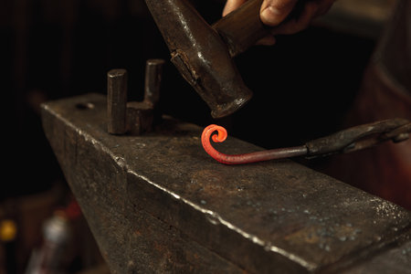 Close-up hands of male blacksmith forge an iron product in a blacksmith. Hammer, red hot metal and...