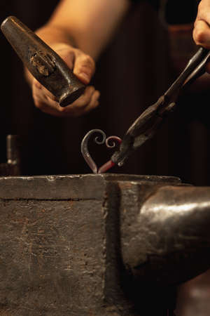 Close-up working powerful hands of male blacksmith forge an iron product in a blacksmith. Hammer, red hot metal and anvil. Concept of labor, retro professionsの写真素材