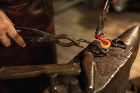 Close-up working powerful hands of male blacksmith forge an iron product in a blacksmith. Hammer,...
