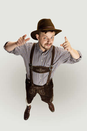 Cute happy bearded man, waiter in traditional Austrian or Bavarian costume standing alone isolated over gray background. Funny meme emotionsの写真素材