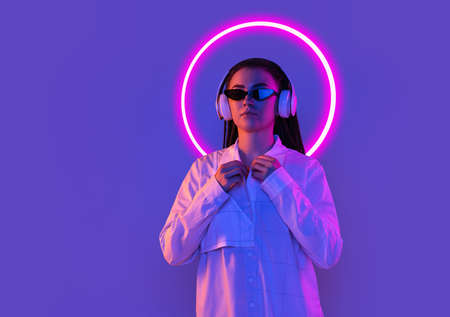 Young womans portrait isolated on blue studio background in multicolored neon light with geometric...