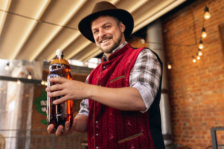 Caucasian bearded man, owner of restaurant in traditional Bavarian festive costume presents craft...