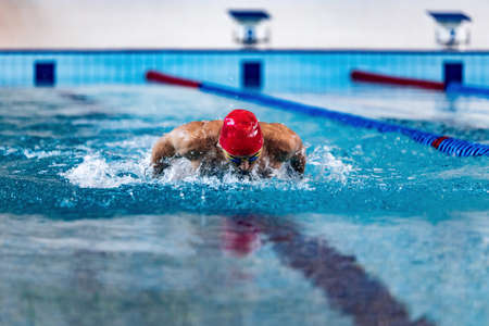 Professional male swimmer in swimming cap and goggles in motion and action during training at pool, indoors. Healthy lifestyle, power, energy, sports movement conceptの写真素材