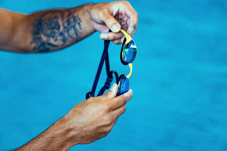 Close-up male hands holding swimming goggles preparing to training at pool, indoors. Healthy lifestyle, power, energy, sports movement conceptの写真素材