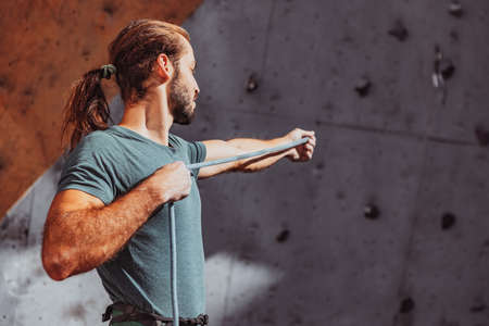 Safety climbing. Young man professional rock climber checking sports equipment before climbing at training center in sunny day, outdoors.の写真素材