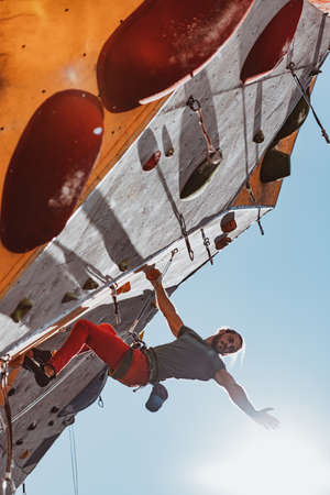 Early morning workouts. One Caucasian man professional rock climber practicing alone at training center in sunny day, outdoors.の写真素材