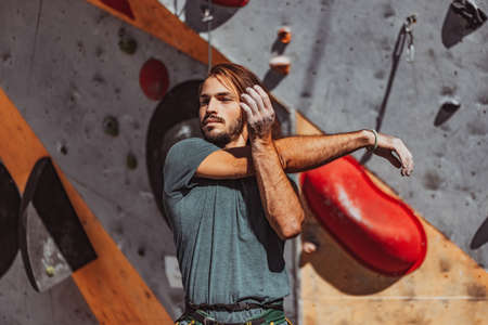 Portrait of Caucasian man professional rock climber warms-up at front of climbing wall at training center in sunny day, outdoors. Concept of healthy lifestyle, sport, motion.の写真素材