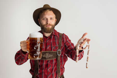 Comic portrait of bearded man in hat and traditional Bavarian costume holding huge mug, glass of...