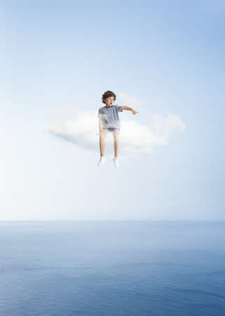 Creative collage with little preschool boy sitting on white cloud and flying at sky, outdoors. Concept of childhood, happiness, dreams, adventureの写真素材