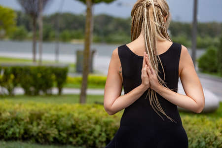 Young beautiful woman with blonde hair doing yoga exercise in green public park in summer morning, outdoors. Healthy lifestyle, mental health concept.の写真素材