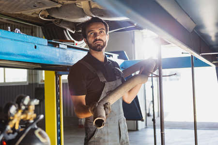 One young man, male auto mechanic, employee in dungarees making car service at garage, indoors....