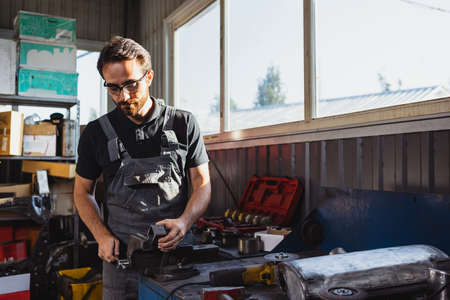 At car service station. One young man, male auto mechanic in dungarees working at car service...
