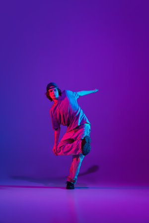 Stylish sportive boy dancing hip-hop in stylish clothes on colorful background at dance hall in neon light. Youth culture, movement, style and fashion, action.の写真素材