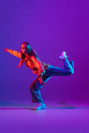 Stylish sportive girl dancing hip-hop in stylish clothes on colorful background at dance hall in neon light. Youth culture, movement, style and fashion, action.の写真素材
