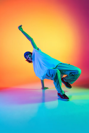Conceptual portrait of young man, hip-hop dancer in stylish clothes in action isolated on colorful background at dance hall in neon light.の写真素材