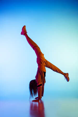 Young sportive girl dancing break dance alone isolated on colorful background at dance hall in neon...