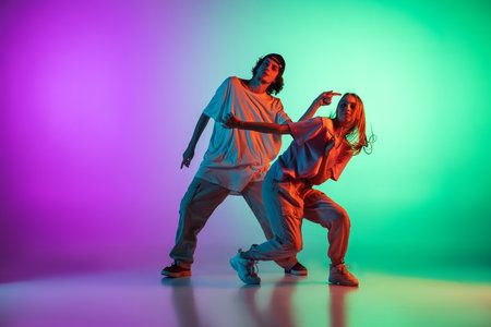Stylish young hip-hop dancers, emotive girl and boy in action and motion in casual sports youth clothes on gradient multi colored background at dance hall in neon light.の写真素材