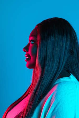 Portrait of African charming woman with long straight hair isolated on blue studio background in...