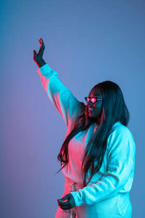 One African beautiful woman with long straight hair isolated on blue studio background in neon light. Concept of human emotionsの写真素材