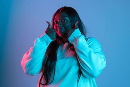 One African beautiful woman with long straight hair isolated on blue studio background in neon...