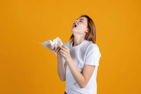 One young girl sneezing, having a runnynose isolated on yellow color studio background. Concept of human emotions, facial expression, health and medicineの写真素材