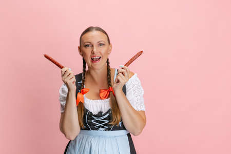 Cute pretty Oktoberfest woman, waitress wearing a traditional Bavarian or german dirndl having fun isolated on pink studio background.の写真素材