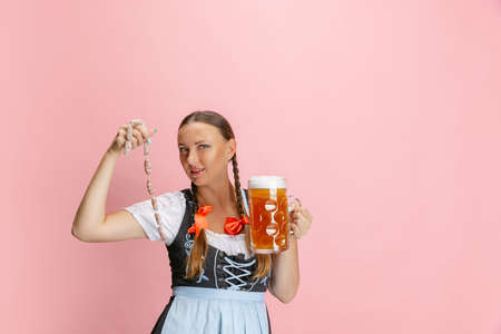 Adorable Oktoberfest woman, waitress wearing a traditional Bavarian or german dirndl holding one liter beer glass isolated on pink studio background.の写真素材
