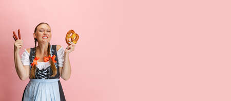 Adorable Oktoberfest woman, waitress wearing a traditional Bavarian or german dirndl holding bretzel isolated on pink studio background. Flyerの写真素材