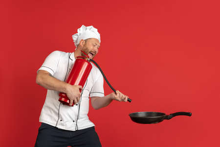 Comic portrait of hadsome bearded man, cook, male chef in white uniform having fun isolated on red studio background. Concept of job, occupation, humor.の写真素材