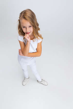 High angle view of beautiful little girl with long hair in modern stylish outfit posing isolated on white studio background. Happy childhood concept.の写真素材