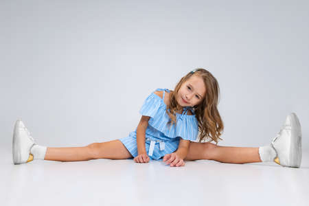 Beautiful little girl in blue holiday outfit sitting on floor isolated on white studio background. Happy childhood concept. Sunny child.の写真素材