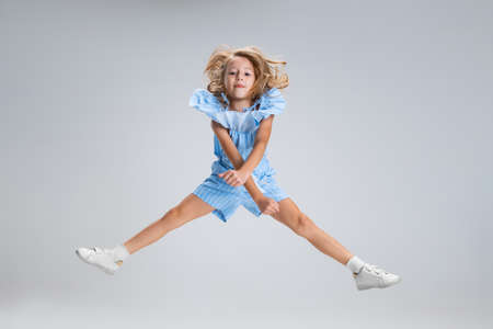Full-length portrait of cute girl in casual clothes jumping isolated on white studio background....