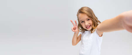 Close-up beautiful little smiling girl with long hair in modern stylish outfit looking at camera isolated on white studio background. Happy childhood concept.の写真素材