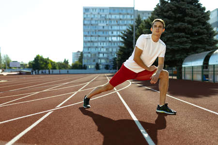 Young Caucasian sportive man, male athlete, runner practicing alone at public stadium, sport court or running track outdoors. Summer sport games.の写真素材