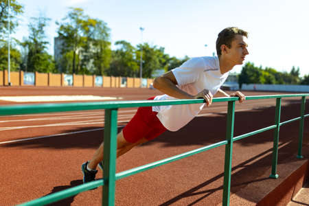 One Caucasian sportive man, male athlete, runner workouts alone at public stadium, sport court or running track outdoors. Summer sport games.の写真素材