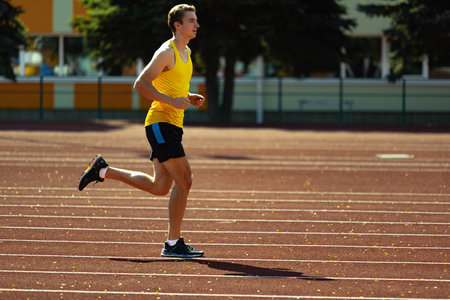 Young Caucasian man, male athlete, runner practicing alone at public stadium, sport court or running track outdoors. Summer sport games.の写真素材