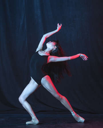 Young and graceful female ballet dancer in motion isolated on dark background in neon light. Art, motion, action, flexibility, inspiration concept.の写真素材