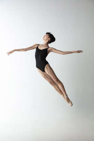 Young and graceful ballet dancer, ballerina dancing isolated on light gray studio background. Art, motion, action, flexibility, inspiration concept.の写真素材