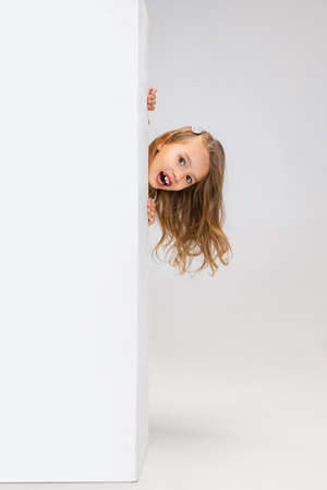 One cute beautiful little girl playing isolated on gray studio background. Human emotions, facial expression concept.の写真素材