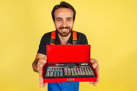 Half-length portrait of smiling young bearded man, male auto mechanic or fitter wearing blue work...