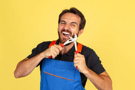 Half-length portrait of smiling young bearded man, male auto mechanic or fitter wearing blue work dungarees isolated over yellow studio background.の写真素材