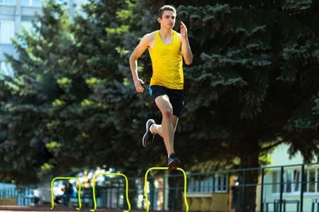 Young Caucasian sportive man, male athlete, runner jumping high at public stadium, sport court or...