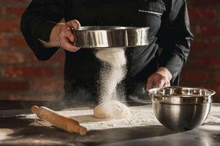 Cropped image of male chef, cook in black kitchen uniform make bread dough at cafe, restaurant...