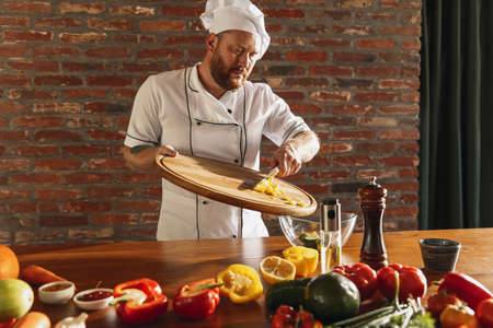 Young Caucasian red-bearded man, chef cooking fresh vegetable salad in cafe, restaurant kitchen. Concept of a correct, healthy diet.の写真素材