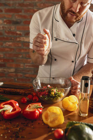Young Caucasian red-bearded man, chef cooking fresh vegetable salad in cafe, restaurant kitchen. Concept of a correct, healthy diet.の写真素材