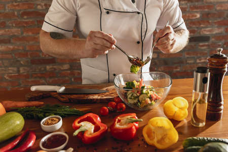 Close-up hands of male chef, cook preparing fresh vegetable salad in his cafe, restaurant kitchen. Concept of a correct, healthy diet.の写真素材