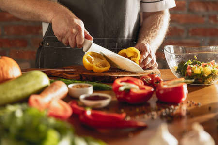 Close-up hands of male chef, cook cutting fresh vegetable salad in his cafe, restaurant kitchen....