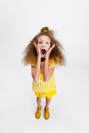 High angle view of little cute curly preschool beautiful girl looking at camera isolated over white studio background.の写真素材